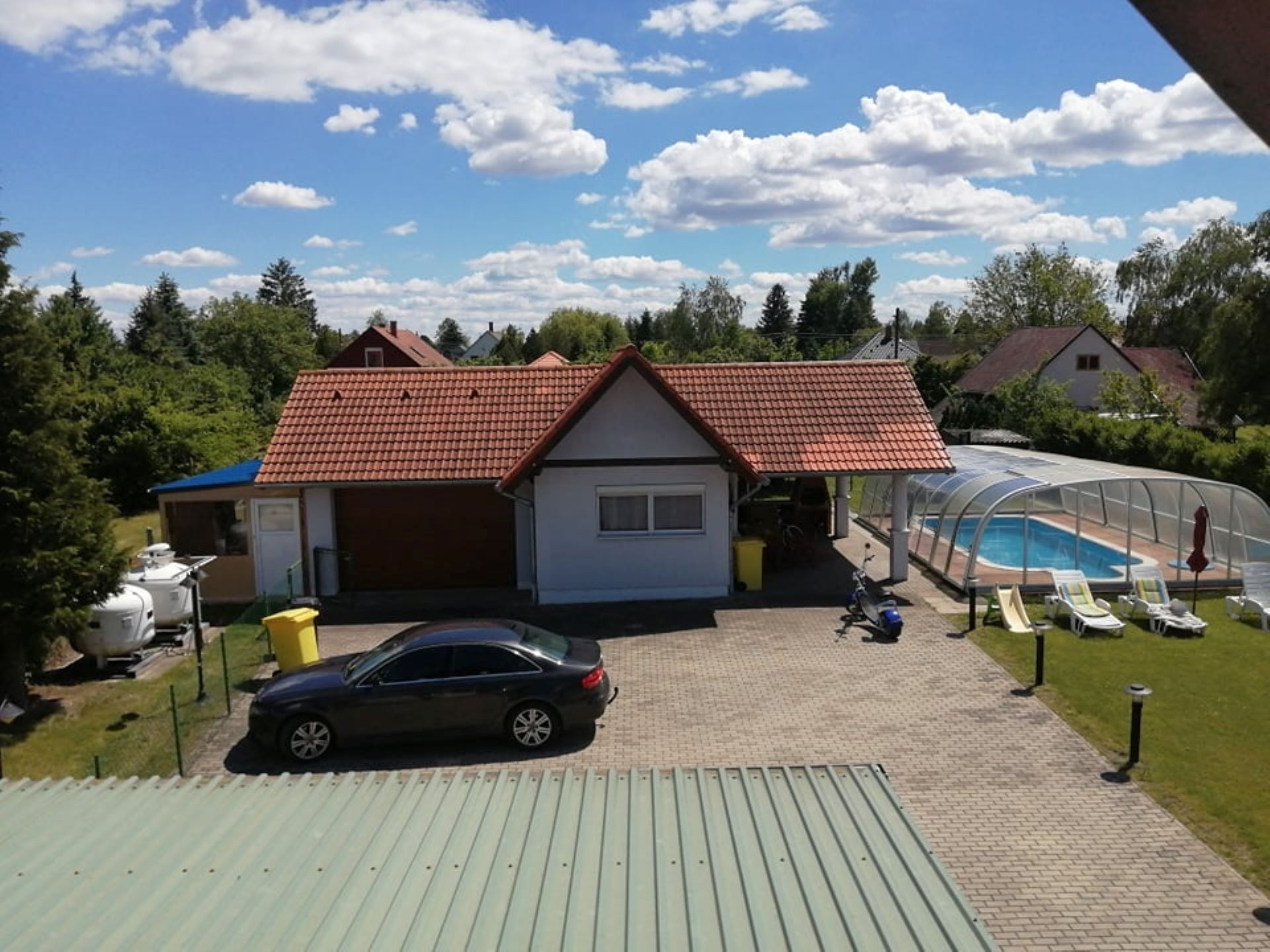 A house with a red-tiled roof, a covered swimming pool, and a car parked in front.