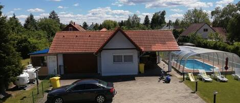A house with a red-tiled roof, a covered swimming pool, and a car parked in front.