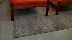 Ein Zimmer mit zwei Holzbetten, grauen Vorhängen und einem gemusterten Teppich.