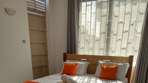 Ein Bett mit hölzernem Gestell, weißer Bettwäsche und orangefarbenen Akzenten.