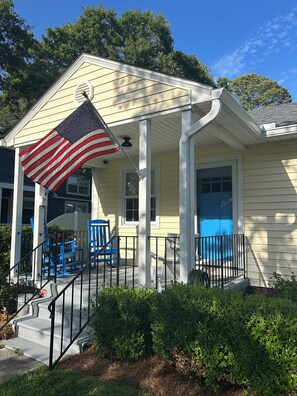Une maison avec un porche, un drapeau et des chaises bleues.