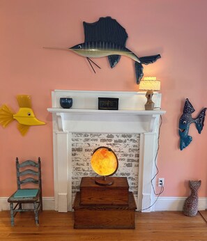 Une pièce avec une cheminée blanche, une lampe en forme de globe, une malle en bois, une chaise et des décorations murales représentant des poissons.