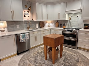 Une cuisine moderne avec des meubles blancs, des appareils en acier inoxydable et un tabouret en bois.
