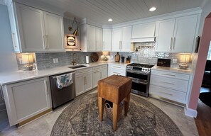Une cuisine avec des armoires blanches, un tabouret en bois, une cuisinière et un évier.