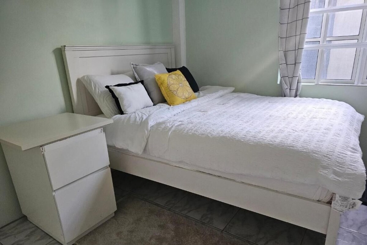 A single bed with a white headboard, a bedside table with drawers, and a window with curtains.