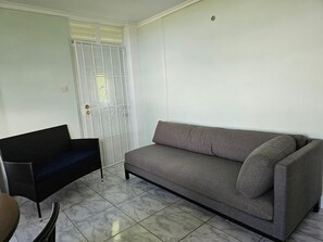 A room with a grey sofa, a black wicker chair, and a white door with a metal gate. - Modern 2-bedroom Apartment near Roseau (Roseau)