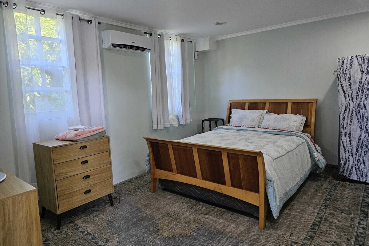 A bedroom with a wooden bed, a bedside table, a dresser, and an air conditioning unit.