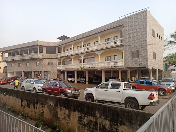 Un edificio de varios pisos con balcones, una tienda en la planta baja y coches aparcados.