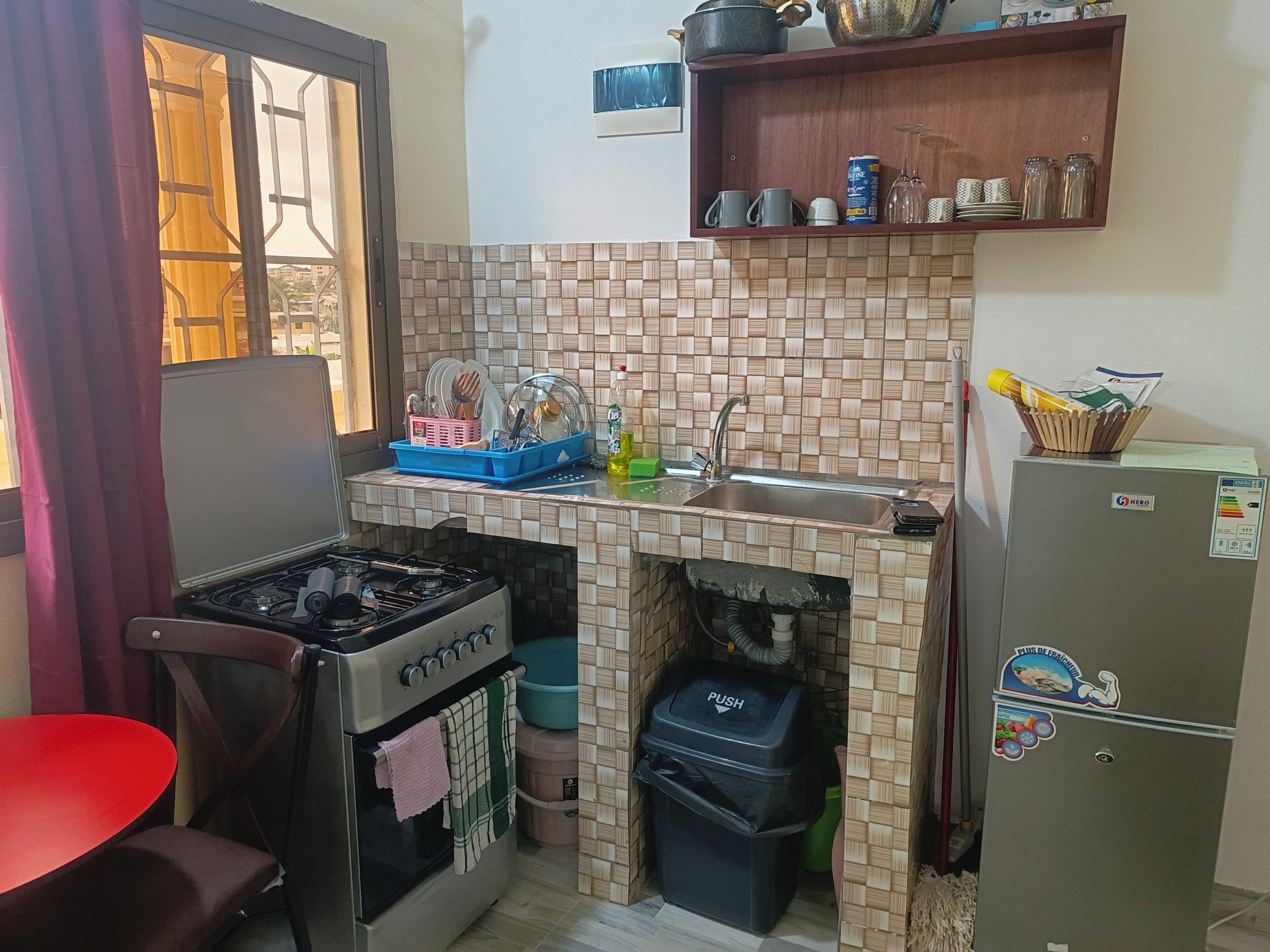 Cocina compacta con estufa a gas, pileta, refrigerador y ventana con vistas.