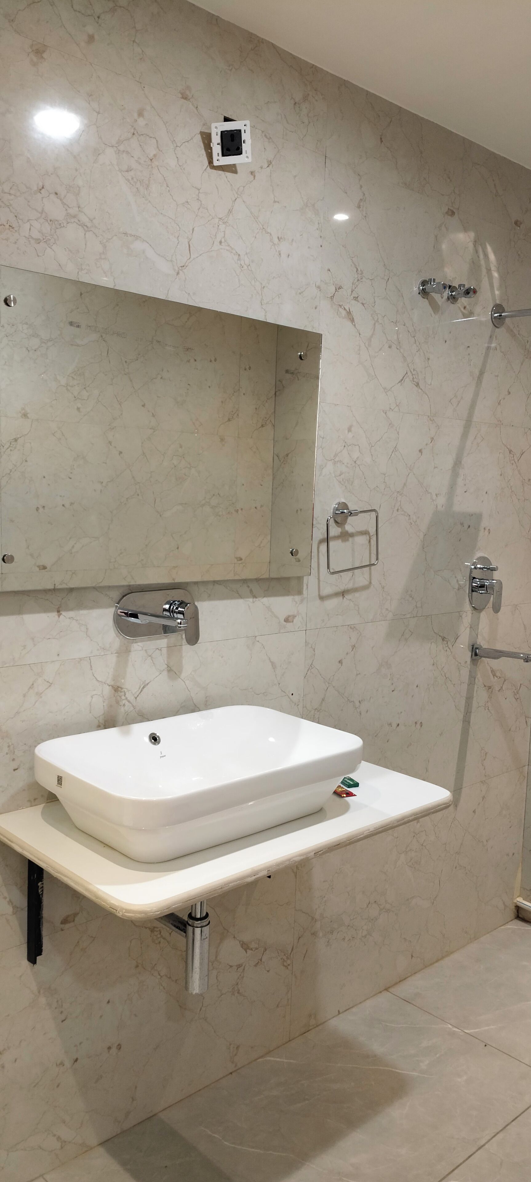 A bathroom with a white sink, a mirror, a shower, and a marble wall.