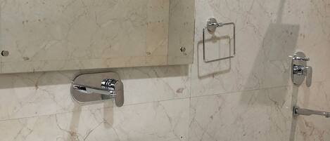 A bathroom with a white sink, a mirror, a shower, and a marble wall.