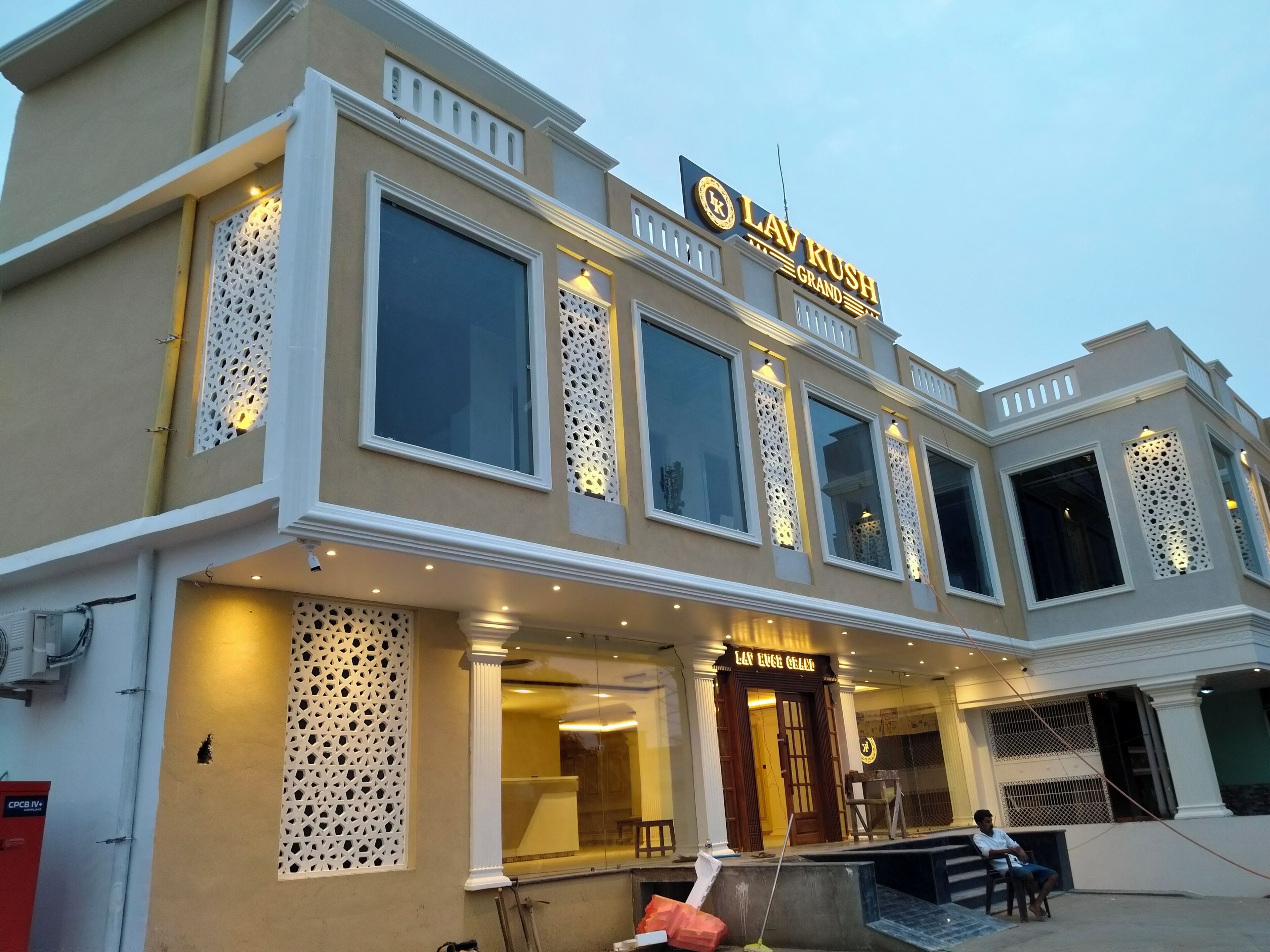 Un hôtel reconnaissable à son enseigne bien visible indiquant « LAV RUSH GRAND HOTEL », à ses grandes fenêtres et à son entrée décorative.