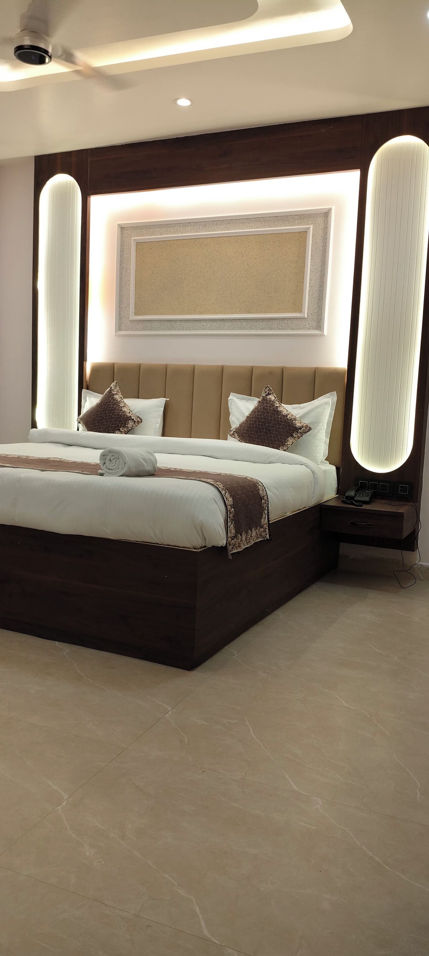 Un dormitorio moderno con una cama grande, una mesita de noche, una lámpara de pared y un ventilador de techo.