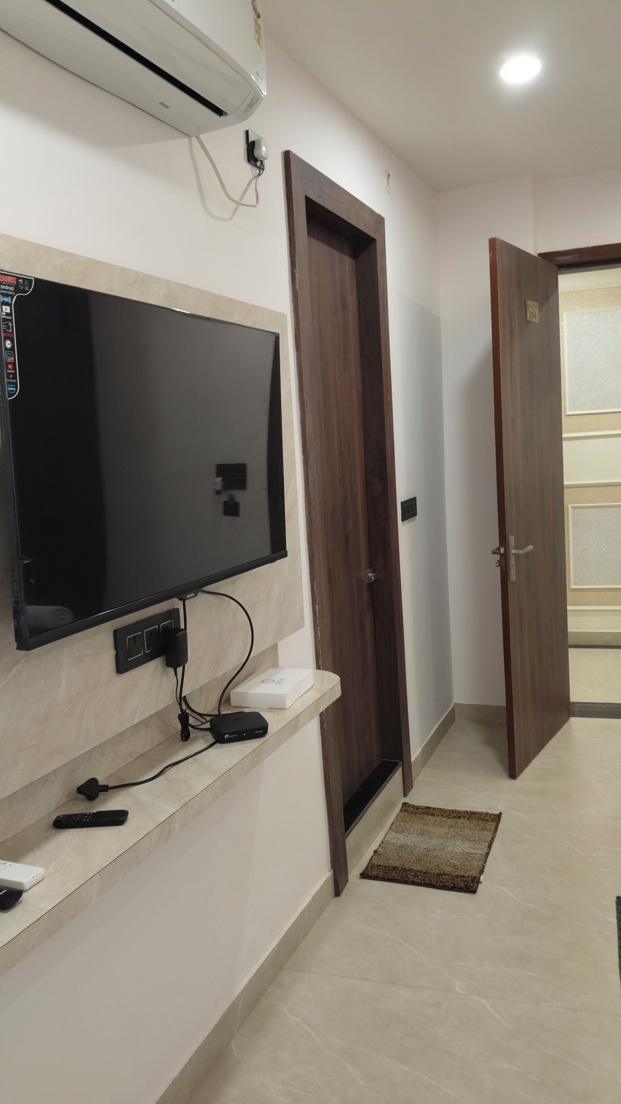 A hallway with a flat-screen TV mounted on the wall, a door, and a tiled floor.