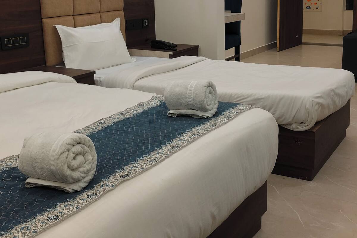 Een hotelkamer met twee bedden, een hoofdeinde, een nachtkastje, een wandklok, een stopcontact en een deur met decoratief paneel.