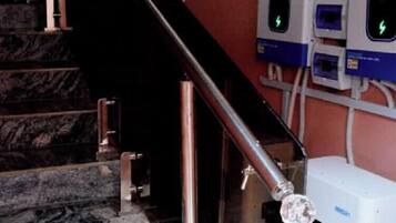 Una escalera con barandillas de metal, un cuadro eléctrico en la pared y un objeto blanco con cubierta transparente.
