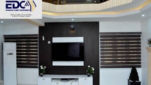A modern living room with a large flat-screen TV, a white entertainment unit, and a decorative plant. - Efeane De-Comfy Apartments. (Magboro)