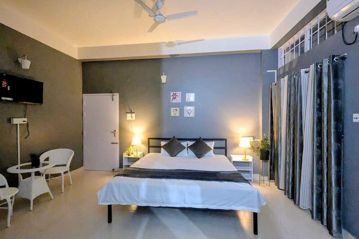 A hotel room with a bed, a TV, a desk, chairs, and a wardrobe.