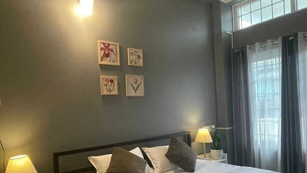Un lit bien fait, avec du linge de lit blanc et deux oreillers, une lampe de chevet, une petite plante en pot et une fenêtre avec des rideaux.