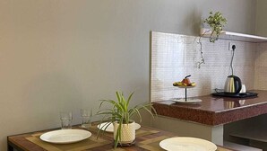 Une table à manger avec quatre assiettes, une plante en pot et un plan de travail de cuisine avec une bouilloire et des fruits.