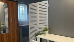 Un coin repas avec une table et des chaises blanches, un meuble en bois et une fenêtre avec des stores.