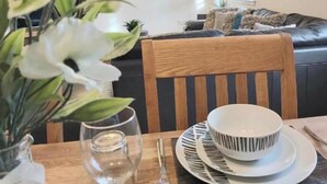 A dining table with a bowl, plate, and glass, a wooden chair, and a sofa in the background. - Inverness City Centre Apartment With elevator (Inverness)