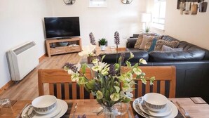 A dining area with a table set for two, a television in the background, and a sofa in the living room. - Inverness City Centre Apartment With elevator (Inverness)