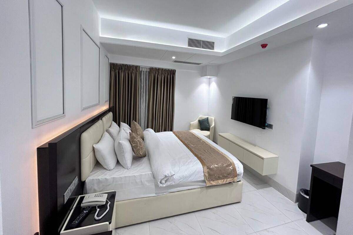 A modern bedroom with a bed, bedside table, TV, and a built-in bench.