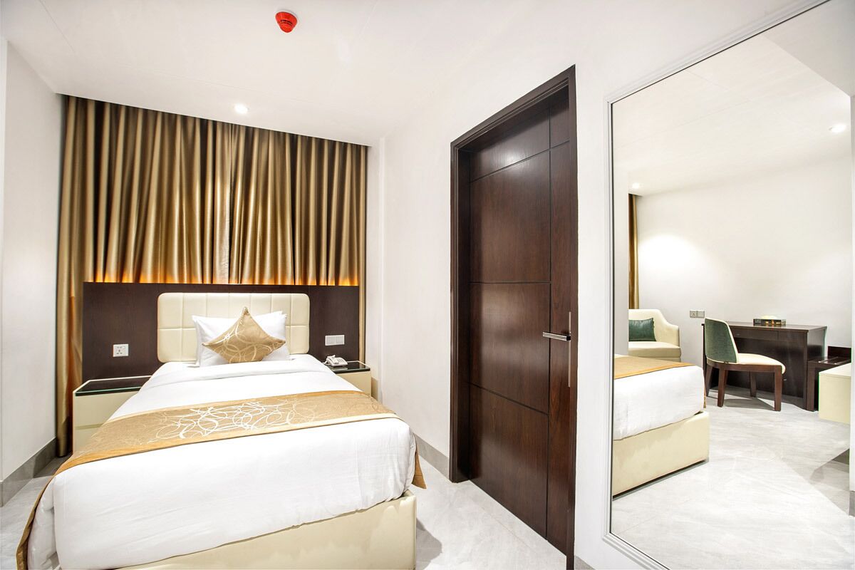 A hotel room with a bed, bedside table, mirror, and a wardrobe.