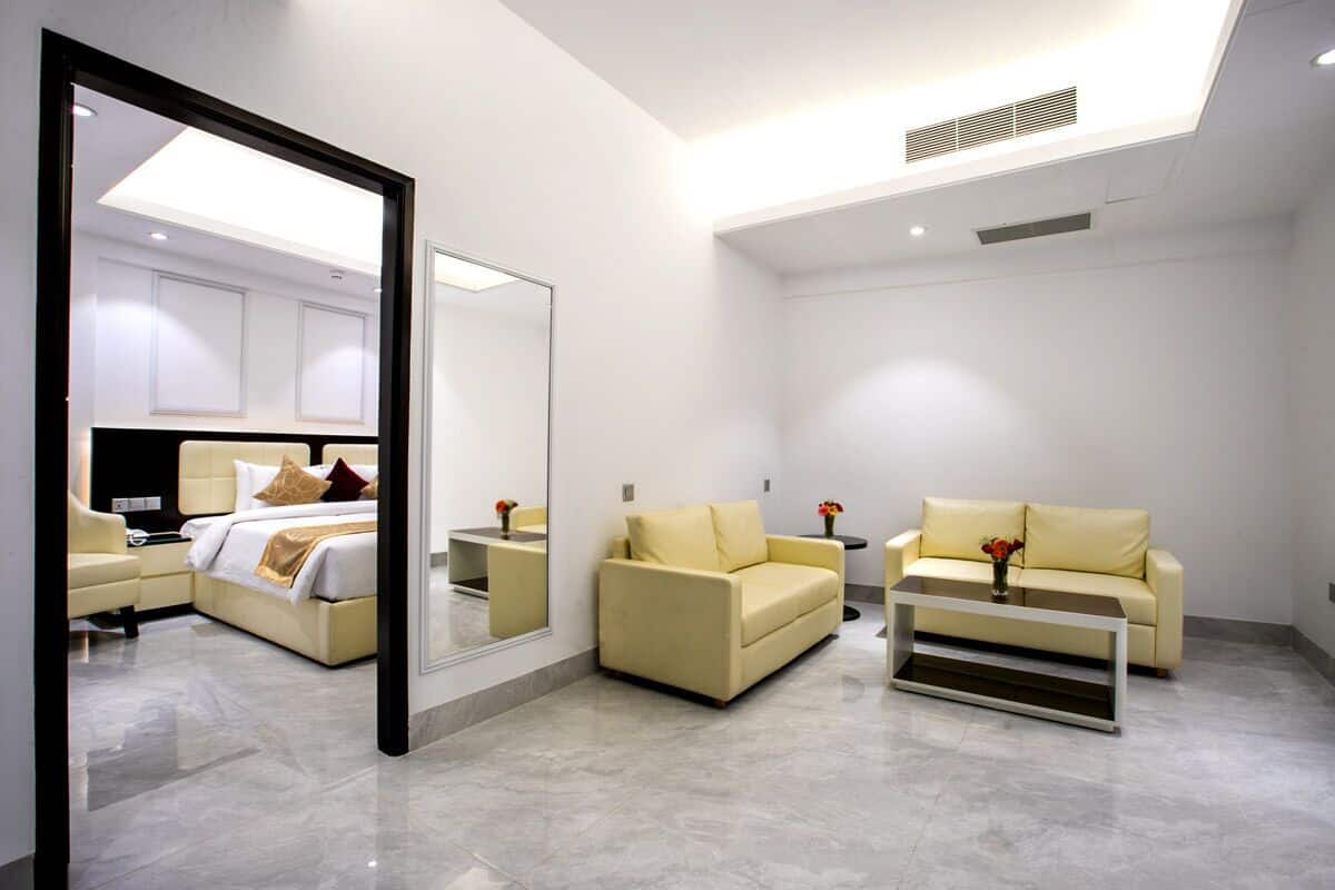 A modern hotel room with a bed, two sofas, a coffee table, and a large mirror.