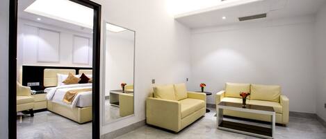 A modern hotel room with a bed, two sofas, a coffee table, and a large mirror.