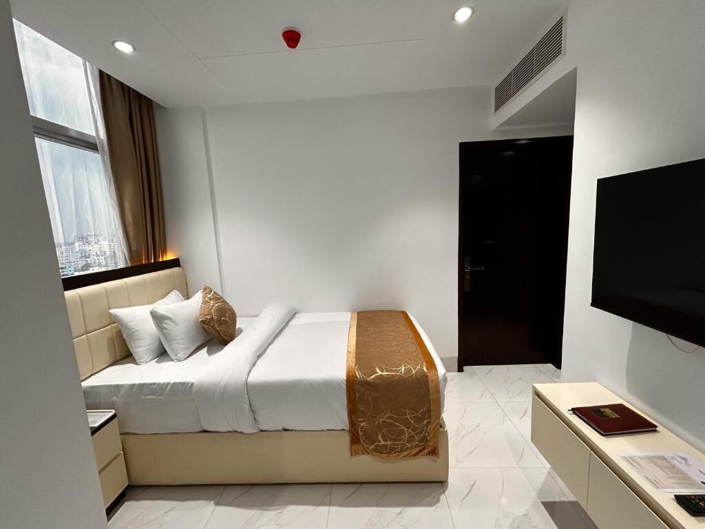 Ein modernes Hotelzimmer mit Bett, Nachttisch, Fernseher und einem Fenster mit Vorhängen.