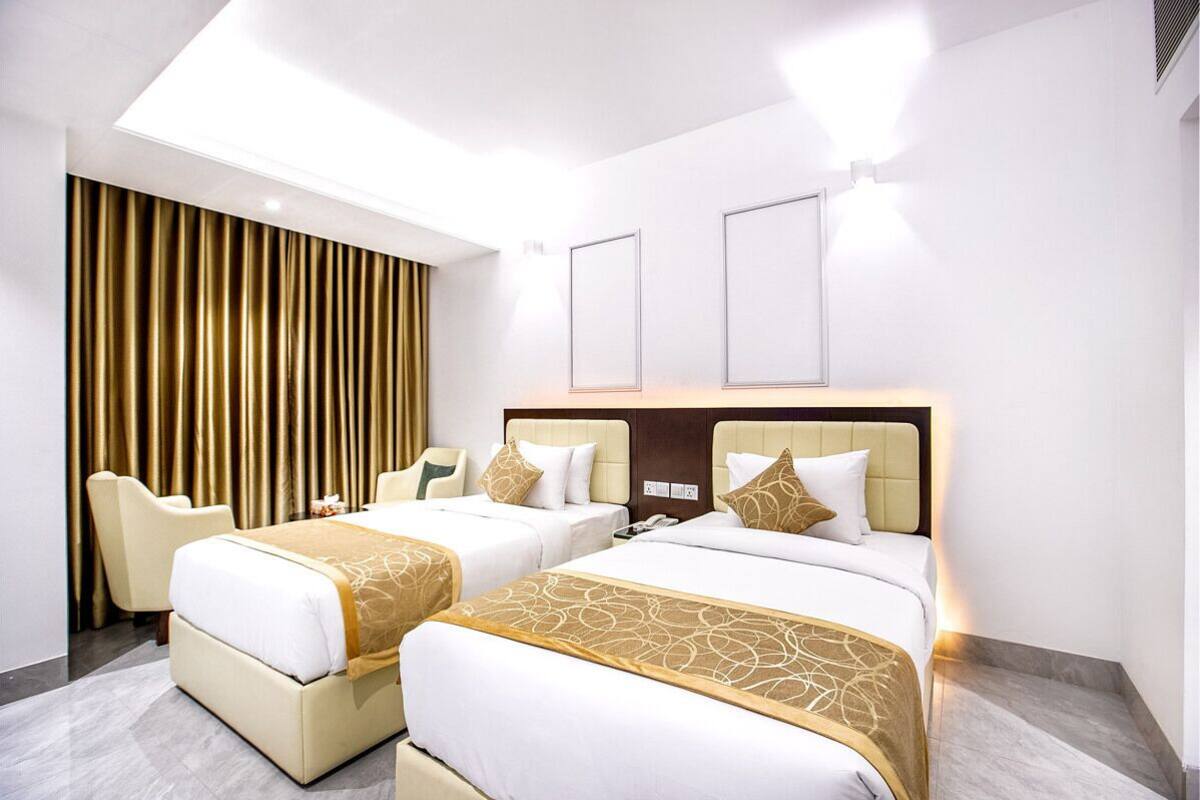 A hotel room with two beds, a large window with curtains, a desk, and a chair.