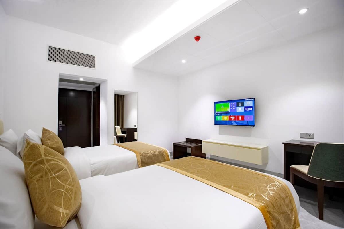 A hotel room with two beds, a desk, a chair, a television, and a door.