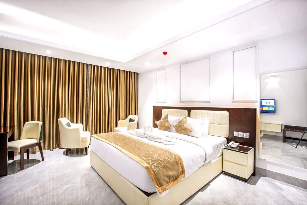 A modern hotel room with a large bed, two chairs, a desk, and a TV.