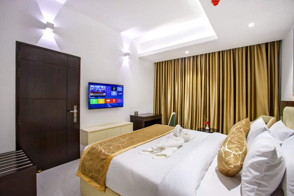 A hotel room with a bed, a television, a desk, and a large window with curtains.