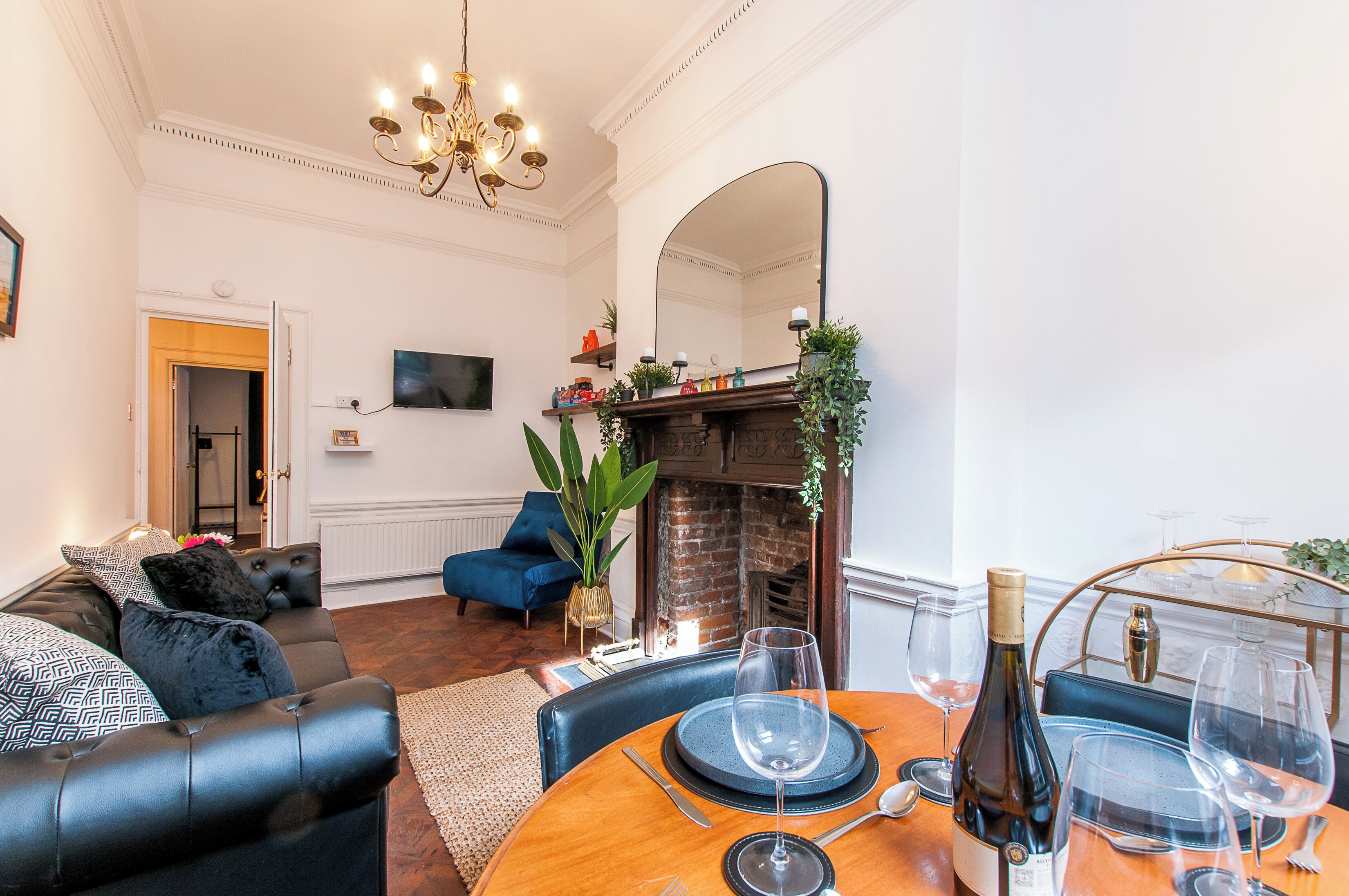 A living room with a fireplace, a dining table set for two, a sofa, and a television mounted on the wall.