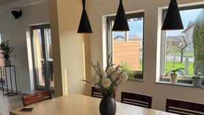 A dining area with a long table, chairs, pendant lights, a vase with flowers, and windows with a view of the outside. - Spacious Family Villa – 4BR, 3Bath Near Airport (Cerklje na gorenjskem)