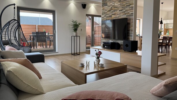 A modern living room with a sofa, coffee table, TV, and a view of the outdoors. - Spacious Family Villa – 4BR, 3Bath Near Airport (Cerklje na gorenjskem)