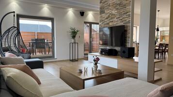 Una sala de estar moderna con sofá, mesa de centro, televisor y vistas al exterior.