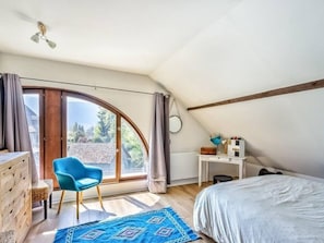 Ein Schlafzimmer mit großem Fenster, Schreibtisch, Stuhl und Bett.