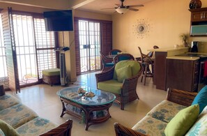 A living room with wicker furniture, a glass coffee table, a television, and a kitchen area. - Casa Hacienda Lujasa: A spacious 3-bedroom home (San Felipe)