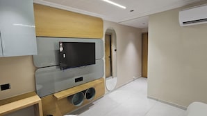Een moderne hotelkamer met een flatscreen televisie bevestigd aan een wand van houten panelen, een ingebouwde airconditioning en een klein houten bijzettafeltje.