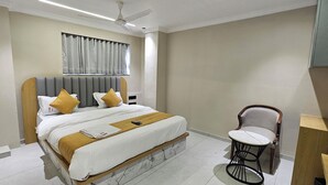 Een hotelkamer met een bed, een stoel, een bureau, een plafondventilator en een raam met gordijnen.