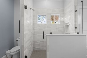 A modern bathroom with a glass-enclosed shower, a toilet, and a vanity with a mirror. - Villa Mojito Main | Gated Lakefront Home (St. Augustine)