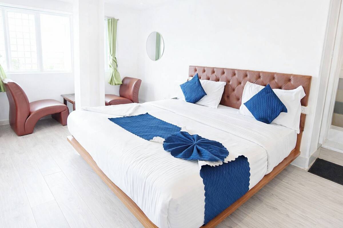 Ein modernes Hotelzimmer mit einem großen Bett, einer Sitzecke mit einem Sessel und Blick ins Freie.