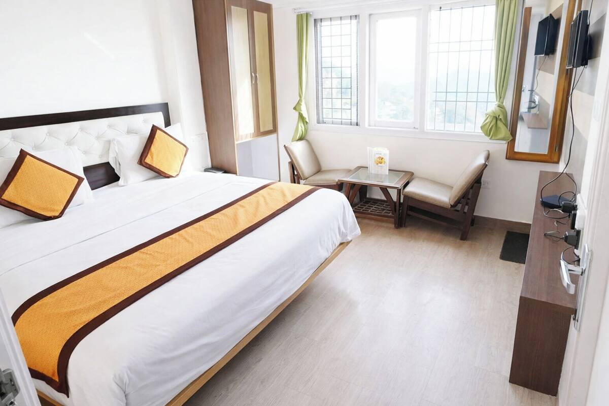 Ein Hotelzimmer mit einem großen Bett, einem kleinen Tisch, einem Stuhl, einem Schreibtisch und einem Vorhangfenster.