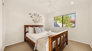 A bedroom with a wooden bed, a decorative wall piece, and a window with a view of greenery. - Palm Beach Escape Steps From Sand (Gold Coast)