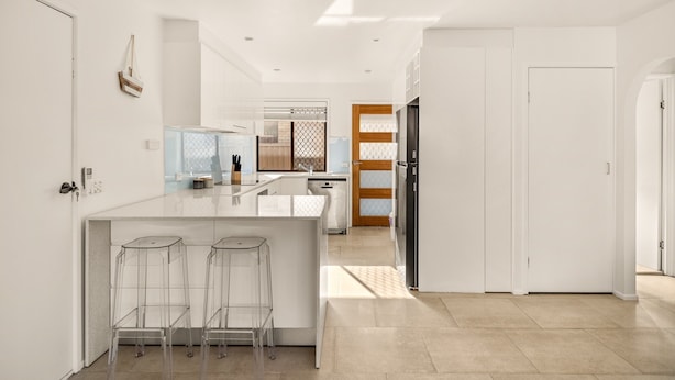 A modern kitchen with a central island, bar stools, and a view into the dining area. - Palm Beach Escape Steps From Sand (Gold Coast)