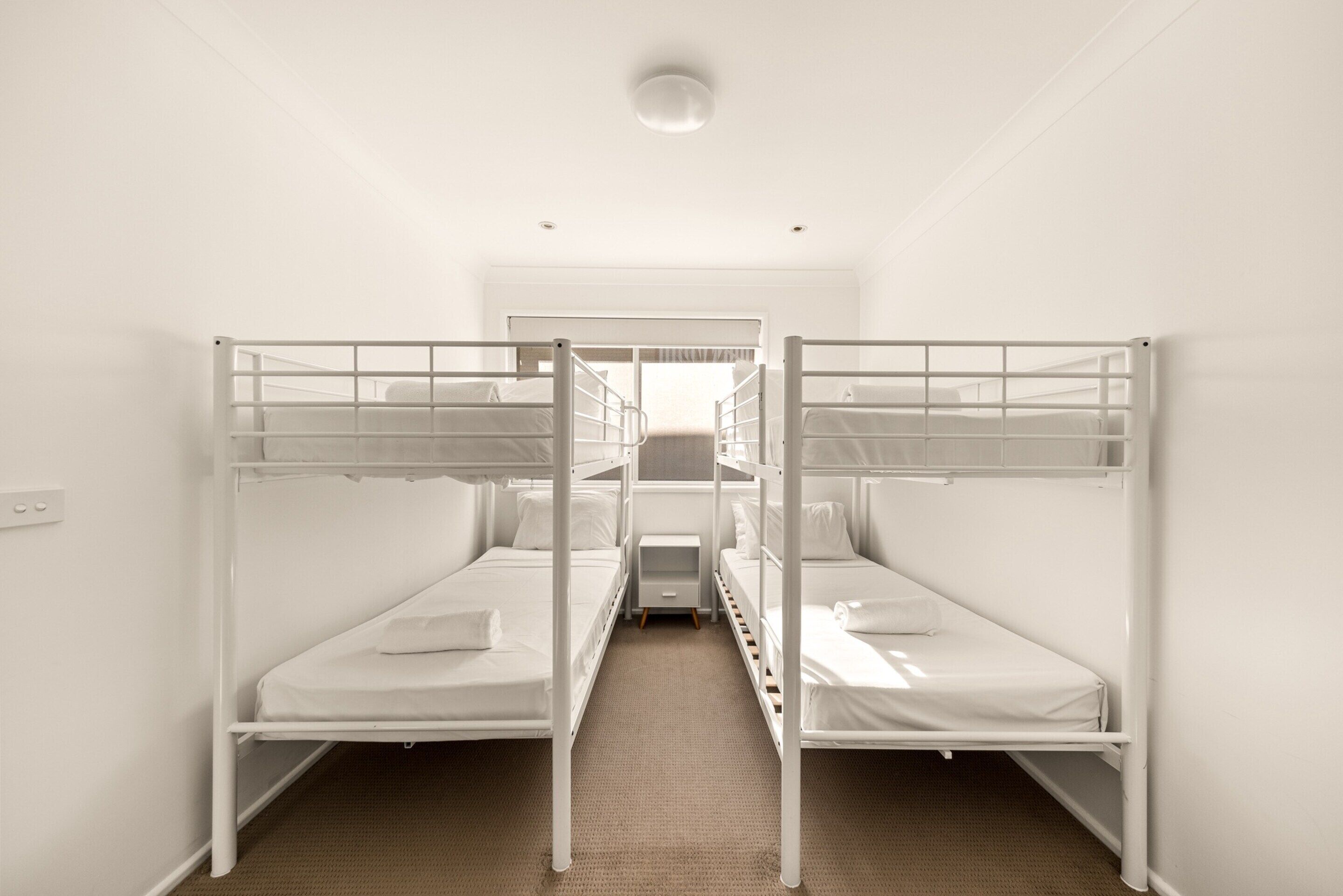 A room with two bunk beds, a small bedside table, and a window with curtains.